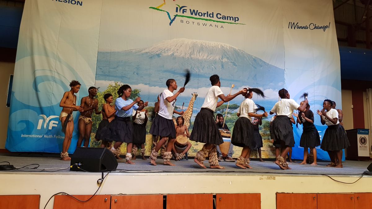 Performers in black and white costumes dancing on the IYF World Camp Botswana stage.