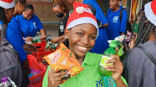 A smiling girl in a Santa hat holding snacks.